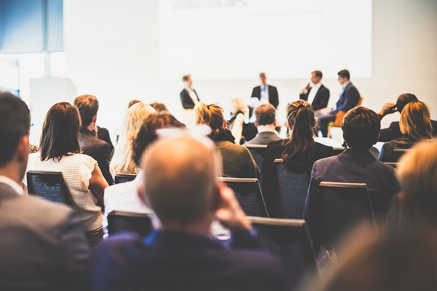 Symbol Menschen im Publikum mit Vortragenden auf der Bühne bei einer Konferenz